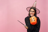 Happy young witch in full costume ready to go trick-or-treating with her bucket for halloween festival, pink background