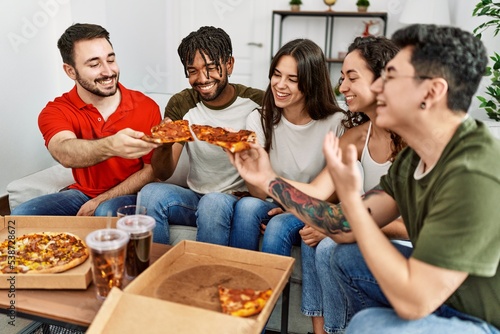 Group of young friends smiling happy eating italian pizza sitting on the sofa at home.