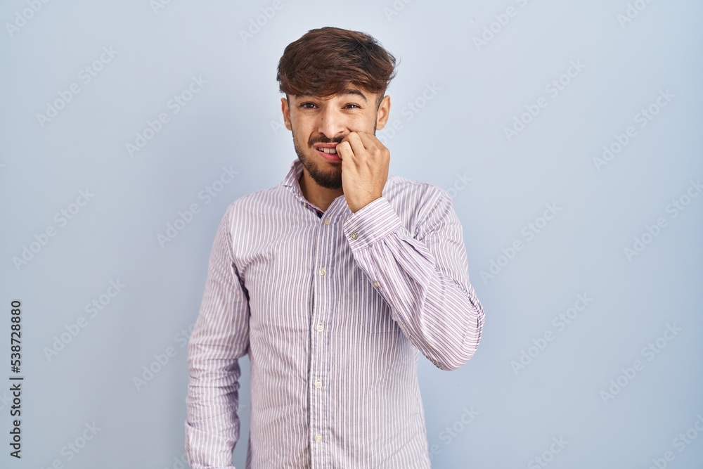 Arab man with beard standing over blue background looking stressed and nervous with hands on mouth biting nails. anxiety problem. Arab man with beard standing over blue background looking stressed and nervous with hands on mouth biting nails. anxiety problem.