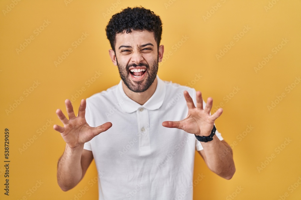 Arab man standing over yellow background smiling funny doing claw gesture as cat, aggressive and sexy expression Arab man standing over yellow background smiling funny doing claw gesture as cat, aggressive and sexy expression