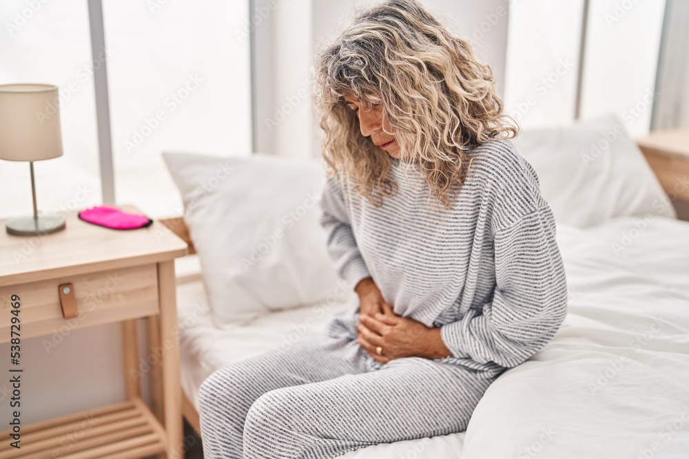 Middle age woman suffering for menstrual pain sitting on bed at bedroom Middle age woman suffering for menstrual pain sitting on bed at bedroom