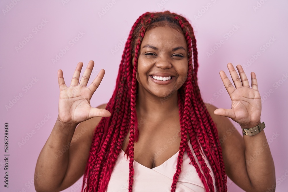 African american woman with braided hair standing over pink background showing and pointing up with fingers number ten while smiling confident and happy. African american woman with braided hair standing over pink background showing and pointing up with fingers number ten while smiling confident and happy.