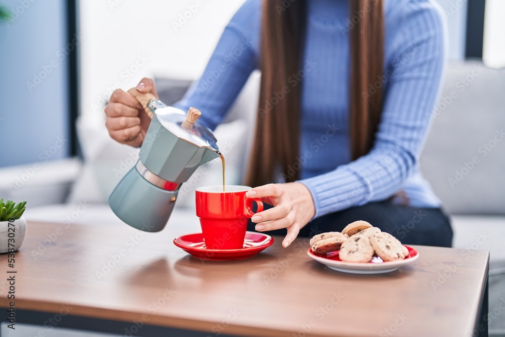 Chinese woman pouring coffee on cup sitting on sofa at home Chinese woman pouring coffee on cup sitting on sofa at home