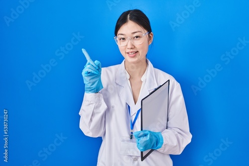 Chinese young woman working at scientist laboratory pointing with hand finger to the side showing advertisement  serious and calm face
