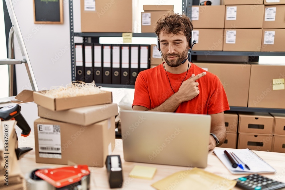 Young hispanic call center agent man working at warehouse pointing with hand finger to the side showing advertisement, serious and calm face Young hispanic call center agent man working at warehouse pointing with hand finger to the side showing advertisement, serious and calm face