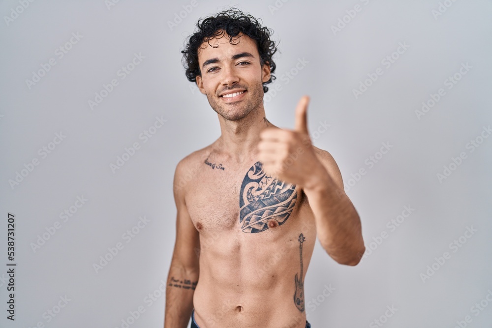 Fototapeta premium Hispanic man standing shirtless doing happy thumbs up gesture with hand. approving expression looking at the camera showing success.
