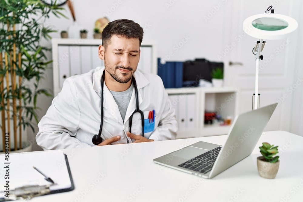 Young doctor working at the clinic using computer laptop with hand on stomach because indigestion, painful illness feeling unwell. ache concept.