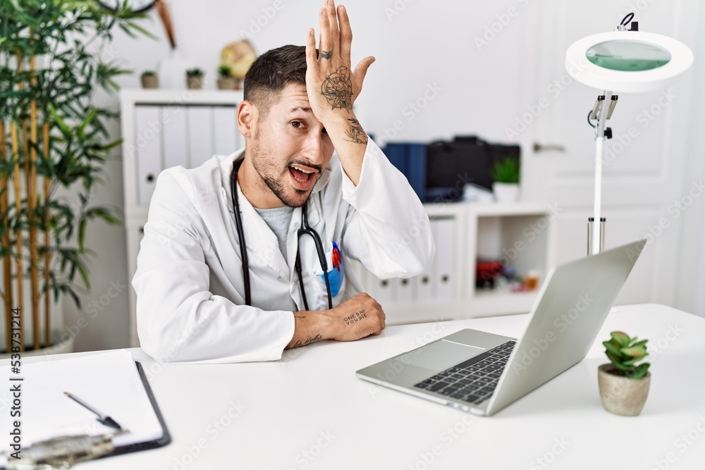 Young doctor working at the clinic using computer laptop surprised with hand on head for mistake, remember error. forgot, bad memory concept. Young doctor working at the clinic using computer laptop surprised with hand on head for mistake, remember error. forgot, bad memory concept.