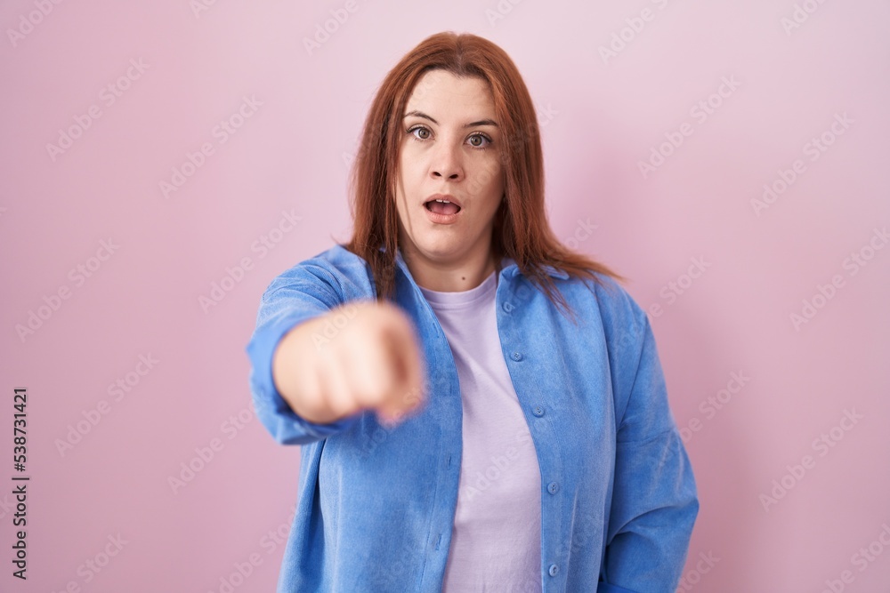 Young hispanic woman with red hair standing over pink background pointing displeased and frustrated to the camera, angry and furious with you Young hispanic woman with red hair standing over pink background pointing displeased and frustrated to the camera, angry and furious with you