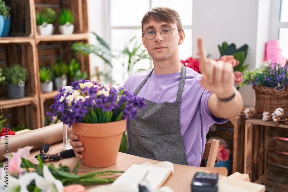 Caucasian blond man working at florist shop pointing with finger up and angry expression, showing no gesture