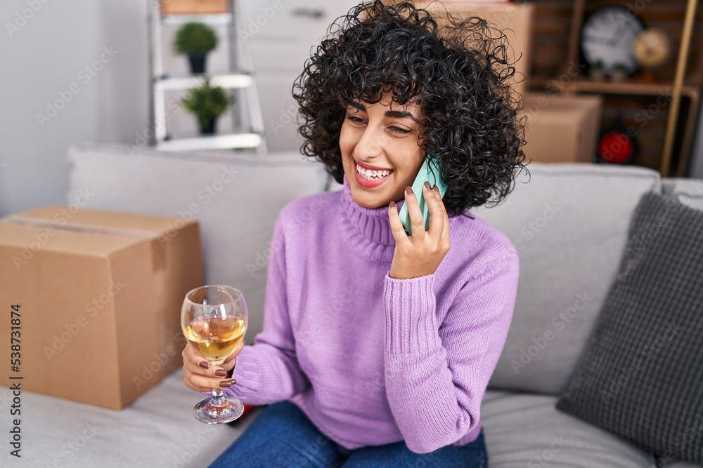 Young middle east woman talking on the smartphone drinking glass of wine at new home Young middle east woman talking on the smartphone drinking glass of wine at new home