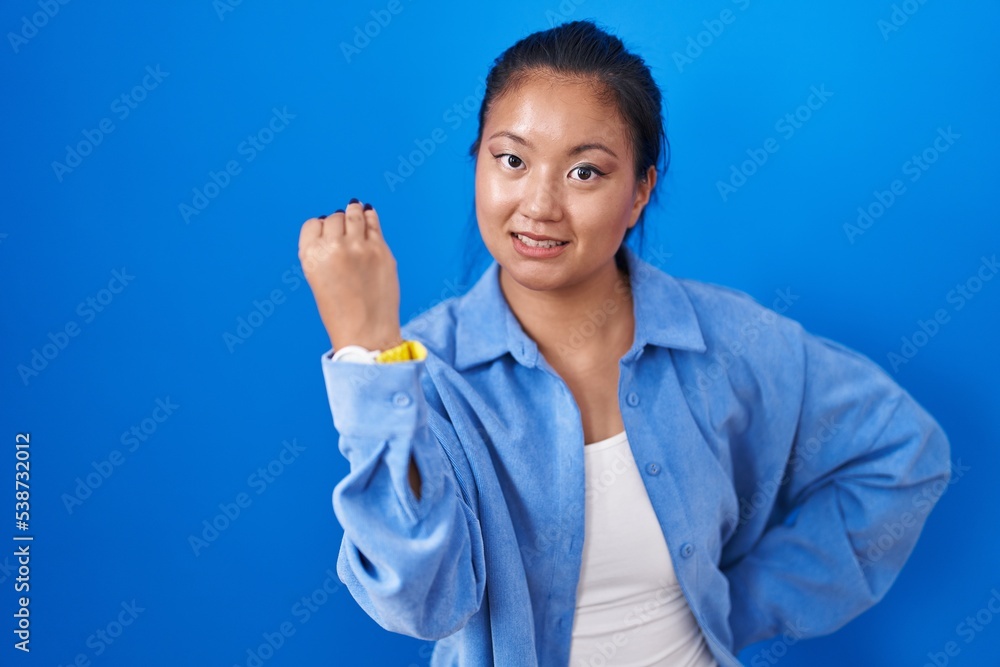 Asian young woman standing over blue background doing italian gesture with hand and fingers confident expression Asian young woman standing over blue background doing italian gesture with hand and fingers confident expression