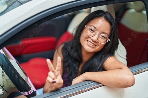 Wallpaper Mural Young chinese woman driving car doing victory gesture with fingers at street Torontodigital.ca