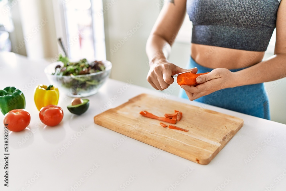 Young woman cutting carrot for salad at kitchen
