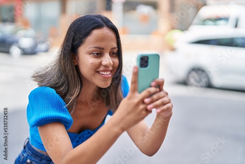 Young hispanic woman smiling confident making photo by the smartphone at street