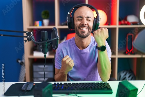 Middle age bald man playing video games wearing headphones celebrating surprised and amazed for success with arms raised and eyes closed © Krakenimages.com