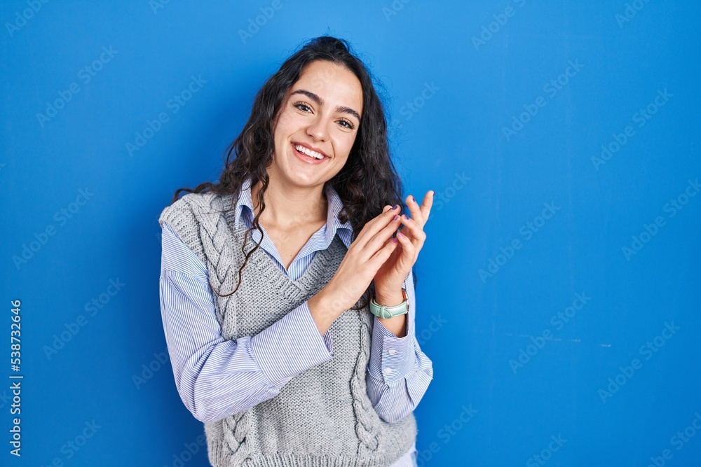 Young brunette woman standing over blue background clapping and applauding happy and joyful, smiling proud hands together Young brunette woman standing over blue background clapping and applauding happy and joyful, smiling proud hands together