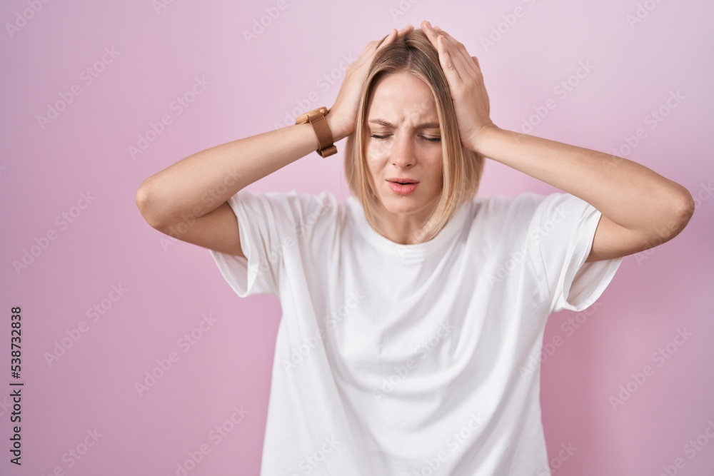 Young caucasian woman standing over pink background suffering from headache desperate and stressed because pain and migraine. hands on head. Young caucasian woman standing over pink background suffering from headache desperate and stressed because pain and migraine. hands on head.