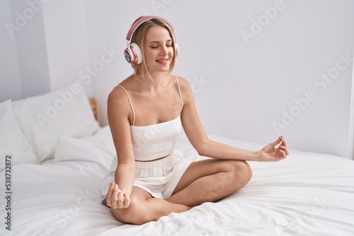 Young blonde woman doing yoga exercise sitting on bed at bedroom