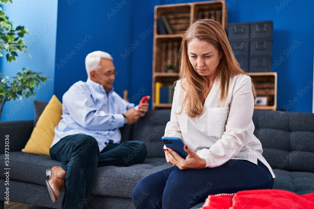 Obraz premium Middle age man and woman couple using smartphone sitting on sofa at home
