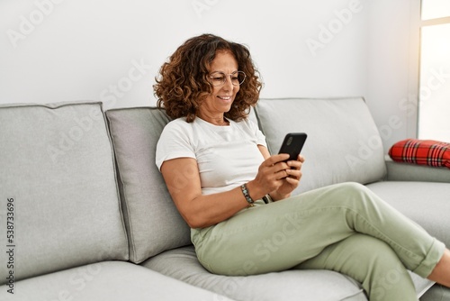 Middle age hispanic woman smiling confident using smartphone at home