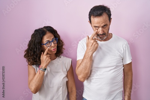 Middle age hispanic couple together over pink background pointing to the eye watching you gesture, suspicious expression