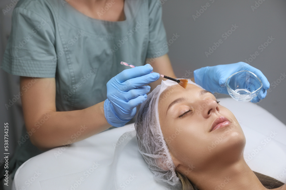 Cosmetologist applying chemical peel product on client's face in salon Cosmetologist applying chemical peel product on client's face in salon