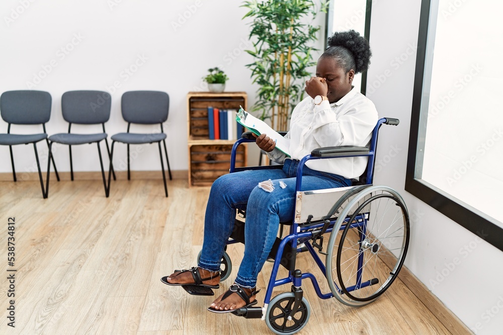 Young black woman sitting on wheelchair at waiting room tired rubbing nose and eyes feeling fatigue and headache. stress and frustration concept. Young black woman sitting on wheelchair at waiting room tired rubbing nose and eyes feeling fatigue and headache. stress and frustration concept.