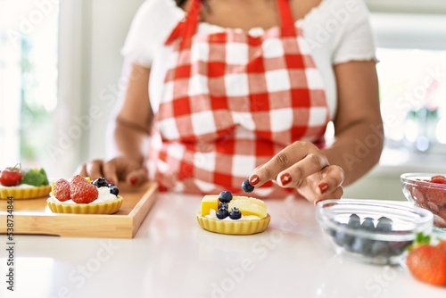 Hispanic brunette woman preparing pastries with fruits at the kitchen