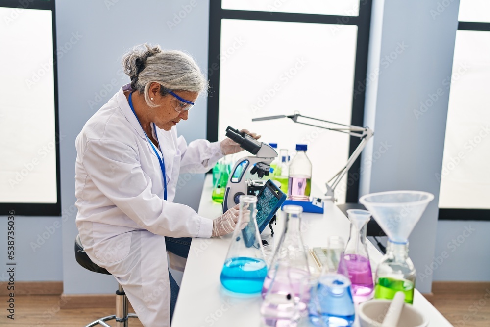 Middle age woman wearing scientist uniform watching embryo on touchpad at laboratory Middle age woman wearing scientist uniform watching embryo on touchpad at laboratory