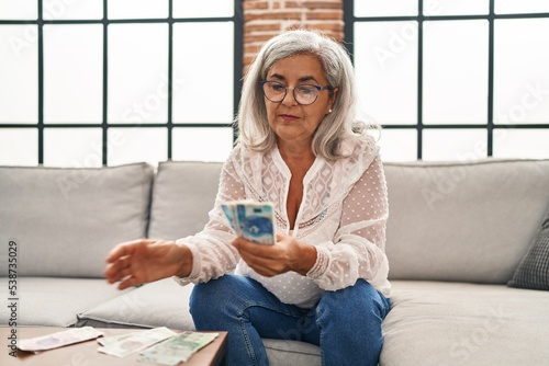 Middle age woman counting sloty banknotes sitting on sofa at home photo