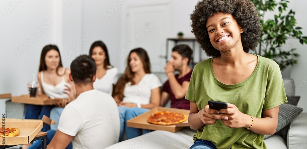 Fototapeta premium Group of young friends eating italian sitting on the sofa. Woman smiling and using smartphone at home.