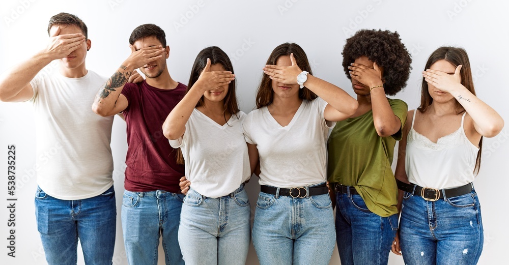 Fototapeta premium Group of young friends standing together over isolated background covering eyes with hand, looking serious and sad. sightless, hiding and rejection concept