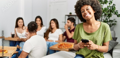 Group of young friends eating italian sitting on the sofa. Woman smiling and using smartphone at home.