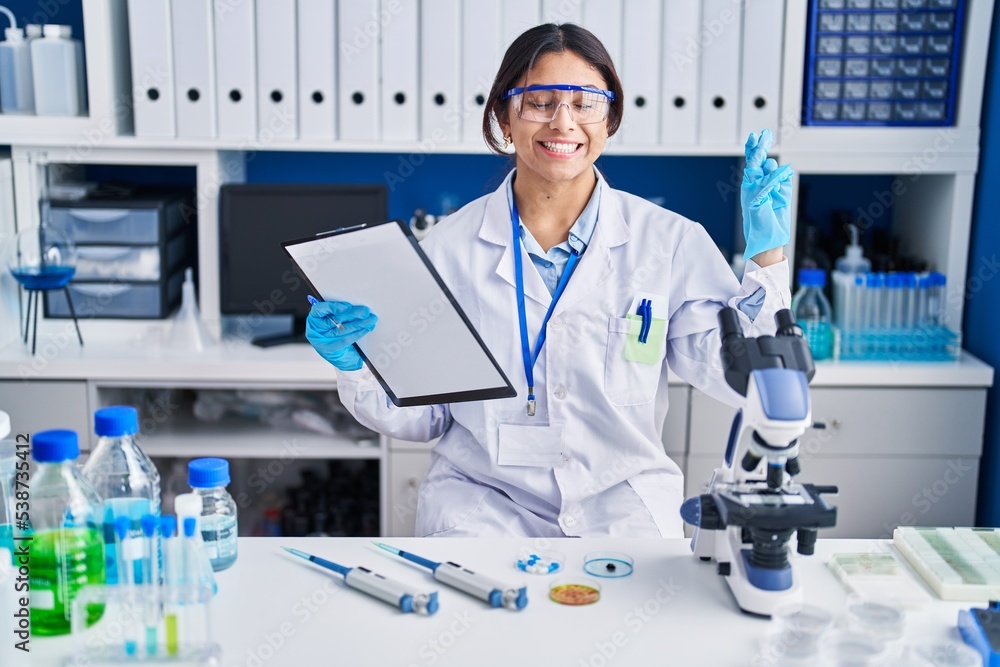 Hispanic young woman working at scientist laboratory gesturing finger crossed smiling with hope and eyes closed. luck and superstitious concept. Hispanic young woman working at scientist laboratory gesturing finger crossed smiling with hope and eyes closed. luck and superstitious concept.