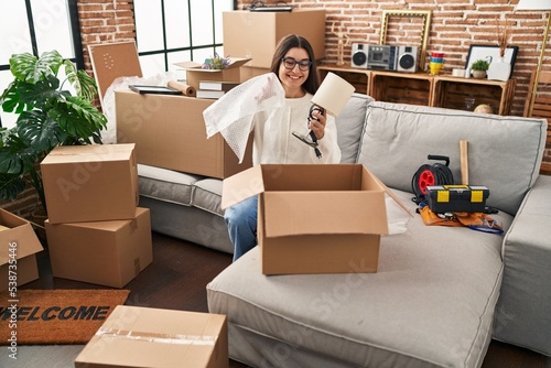 Young hispanic woman smiling confident unpacking cardboard box at new home