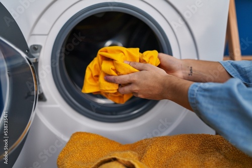Young hispanic woman washing clothes at laundry room