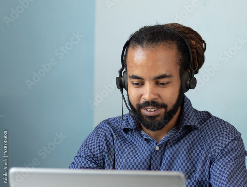 Smiling Latin American man in headset watch webinar or training on modern computer,
 happy biracial male call center agent or telemarketer work consult client online,
 good customer service concept photo