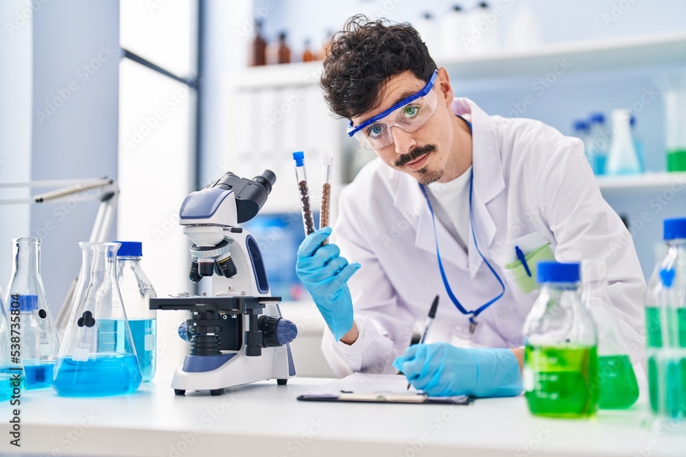 Fototapeta premium Young caucasian man scientist writing report holding test tubes at laboratory