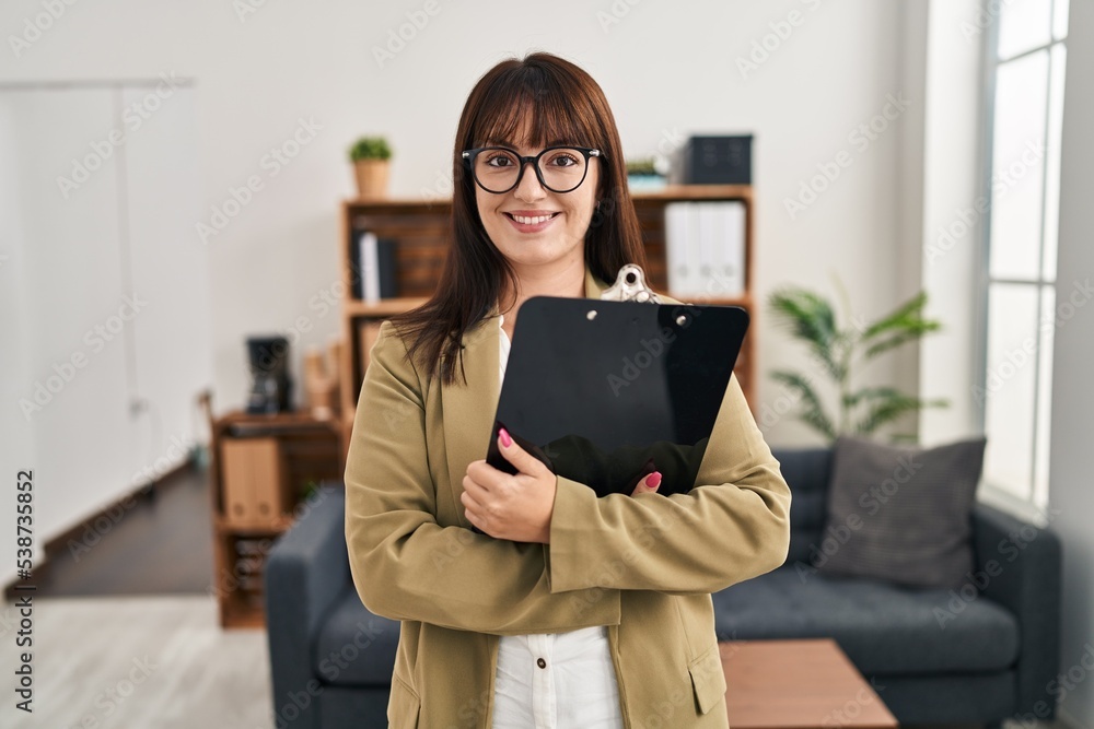 Young beautiful hispanic woman business worker smiling confident holding clipboard at office Young beautiful hispanic woman business worker smiling confident holding clipboard at office