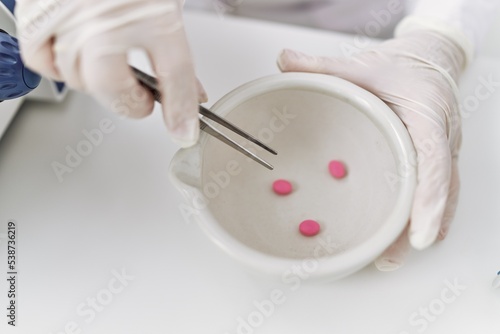 Senior grey-haired woman wearing scientist gloves holding pill at laboratory