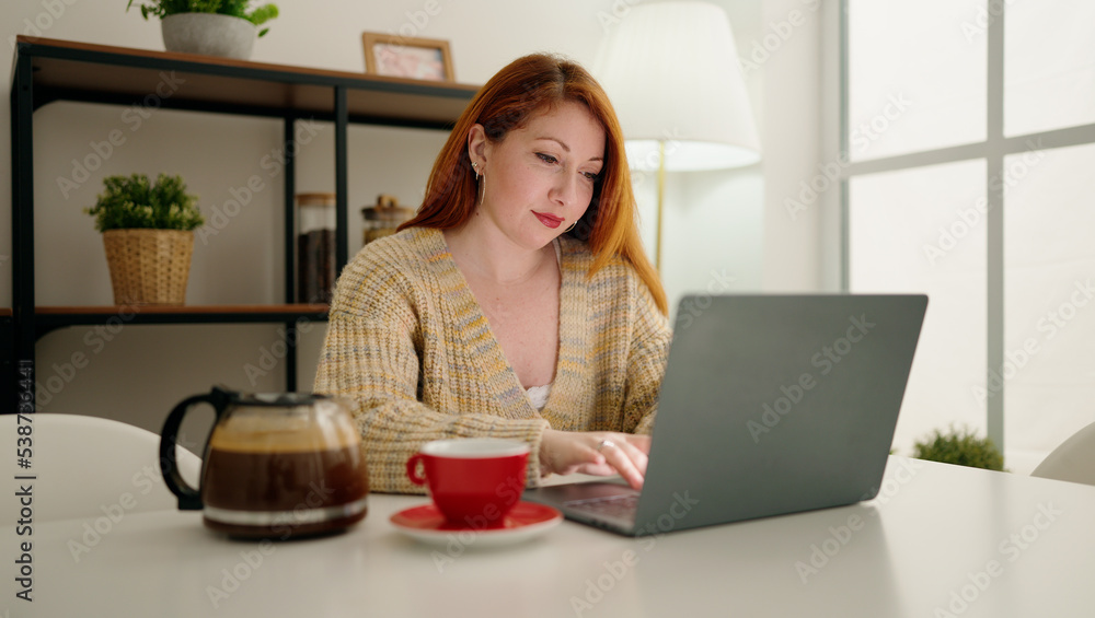 Young redhead woman using laptop drinking coffee at home Young redhead woman using laptop drinking coffee at home