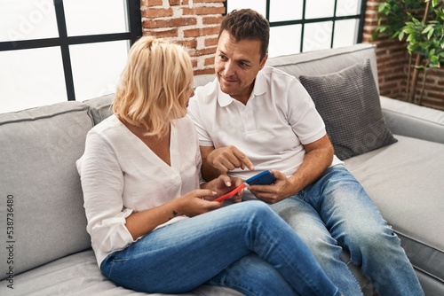Middle age man and woman smiling confident using smartphone at home