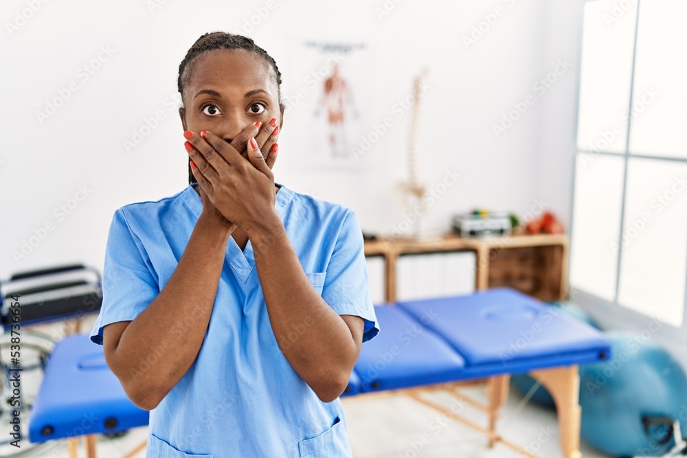 Black woman with braids working at pain recovery clinic shocked covering mouth with hands for mistake. secret concept.