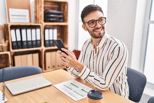 Young hispanic man business worker smiling confident using smartphone at office