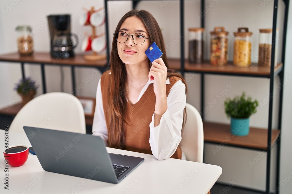Young beautiful hispanic woman using laptop and credit card sitting on table at home Young beautiful hispanic woman using laptop and credit card sitting on table at home