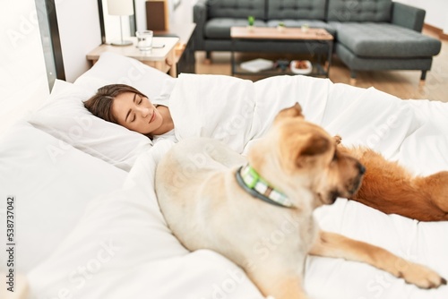 Young hispanic woman sleeping lying on bed with dogs at bedroom