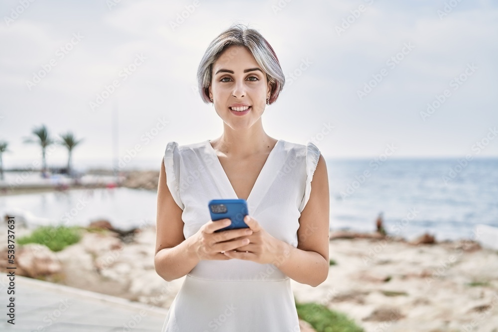 Young caucasian girl smiling happy using smartphone at the beach.