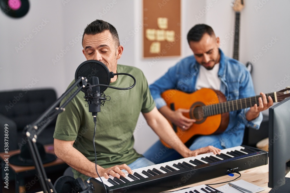 Two men musicians singing song playing piano and classical guitar at music studio Two men musicians singing song playing piano and classical guitar at music studio
