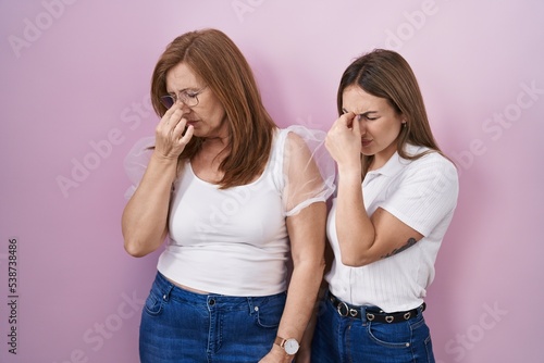 Hispanic mother and daughter wearing casual white t shirt over pink background tired rubbing nose and eyes feeling fatigue and headache. stress and frustration concept.